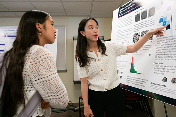 A student shows another student something on their research poster.