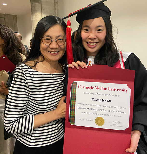 Claire Su wearing regalia and holding a certificate, posing with her mother