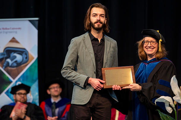  Ian Martin accepts an award plaque from a professor wearing regalia