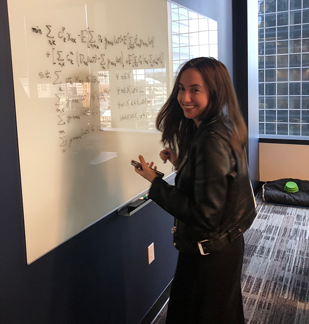 Cristiana Lara turns and smiles while writing equations on a whiteboard in an office