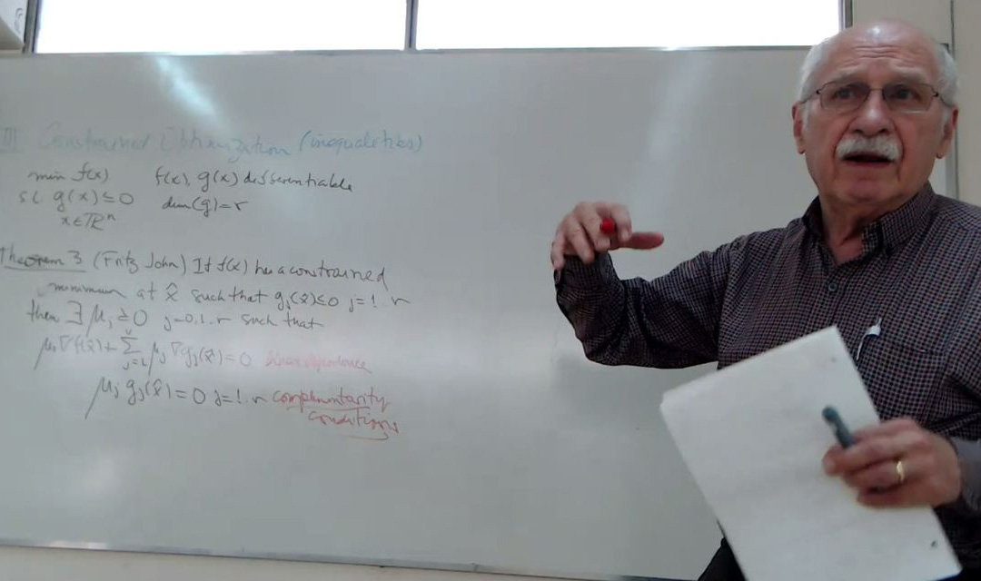 Ignacio Grossmann speaking and gesturing in front of a whiteboard with equations on it