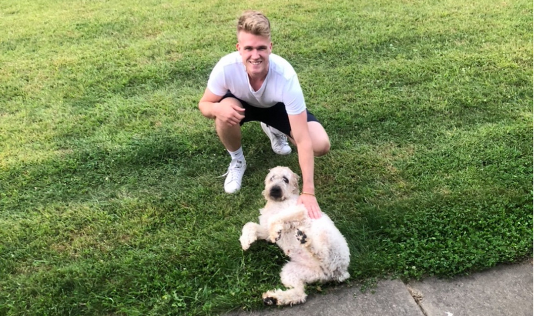 Dennis Loevlie squats down next to a white dog laying on grass