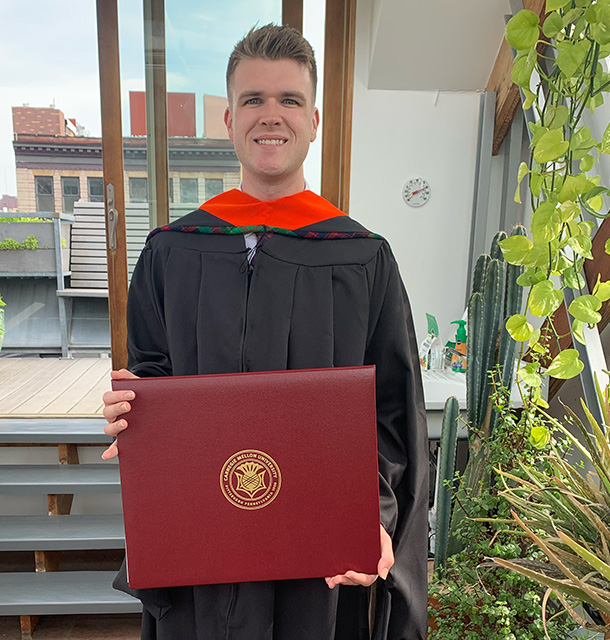 Dennis Loevlie wearing master’s regalia and holding his diploma