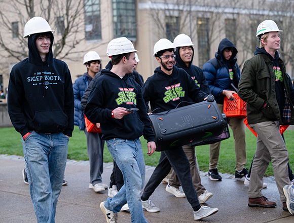 A group of young men wearing matching hoodies and white hard hats, walking on a sidewalk.