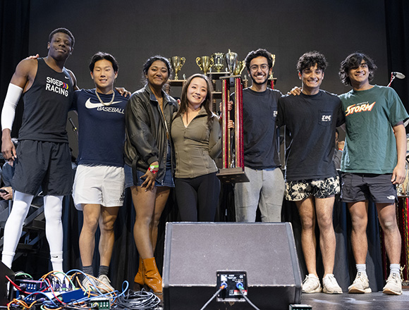 Seven college students pose for a photo holding a large trophy.