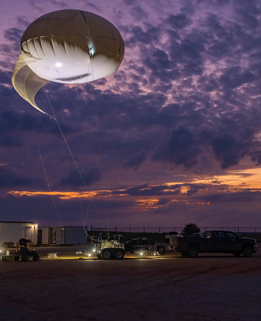 The white tethered balloon flies in an orange sky with purple clouds.