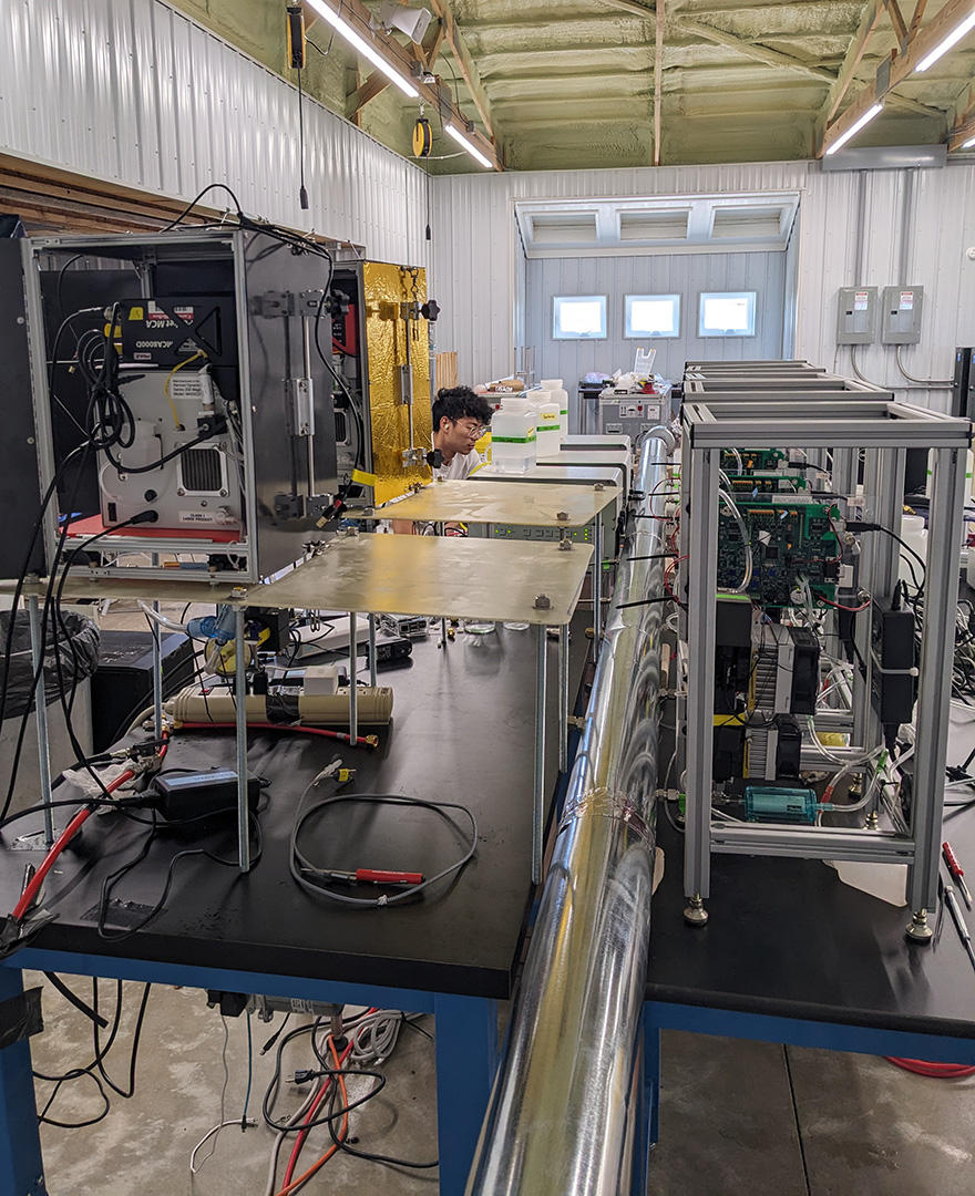 In the foreground, two tables filled with scientific instruments. In the background, a man sits working intently.