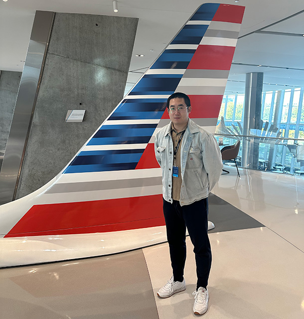 Yingkai Song stands in front of a plane tail painted with American Airlines branding, inside a modern office atrium.