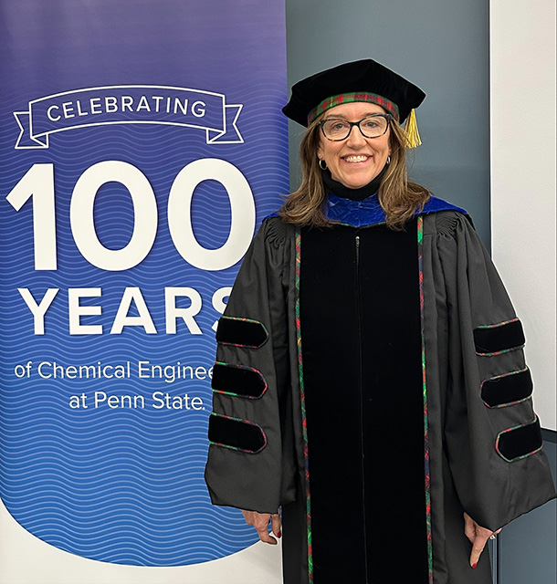 Stephanie Butler Velegol wears her Ph.D. graduation regalia while standing next to a sign that says “Celebrating 100 years of Chemical Engineering at Penn State.”