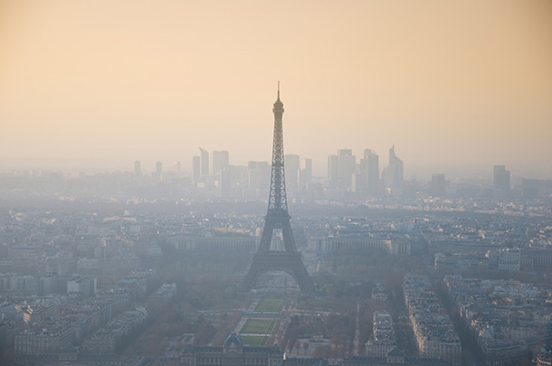 The Paris skyline, with the Eiffel Tower in the center, seen through fog. In the background, the sky glows a soft, hazy gold.