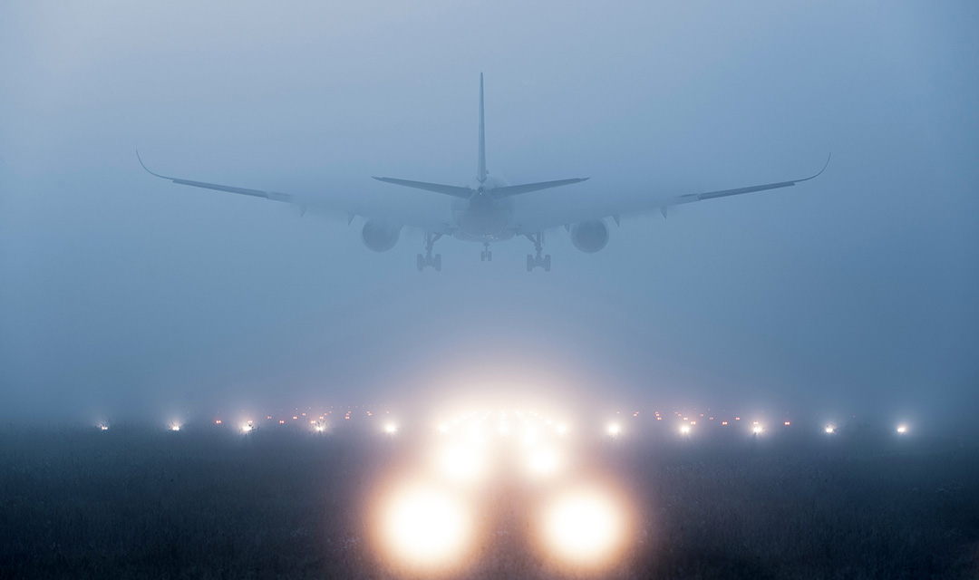 An airplane landing on a runway in heavy fog. The lights along the runway are blurry through the fog.