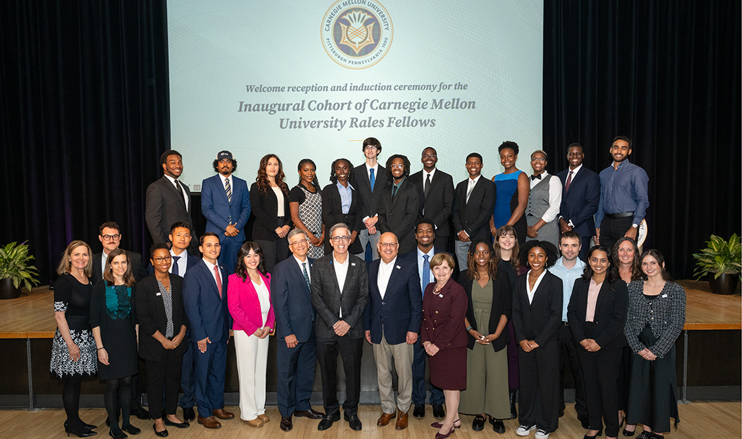 Two rows of adults dressed in business attire pose for a group photo in front of a screen on which is displayed “Inaugural cohort of Carnegie Mellon University Rales Fellows.”